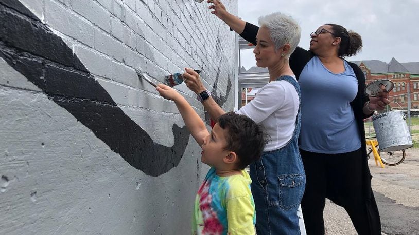 Braylon Bettinger, age 4, his grandmother Jessica Bettinger and Amber Vanderpool were part of a group of volunteers who gathered to paint a new mural on the back of the State Theater in downtown Springfield on Thursday morning. The mural sight was a filming location for an ABC Disney pilot being shot here, and Disney worked with the Springfield Public Arts Committee to create the mural here.