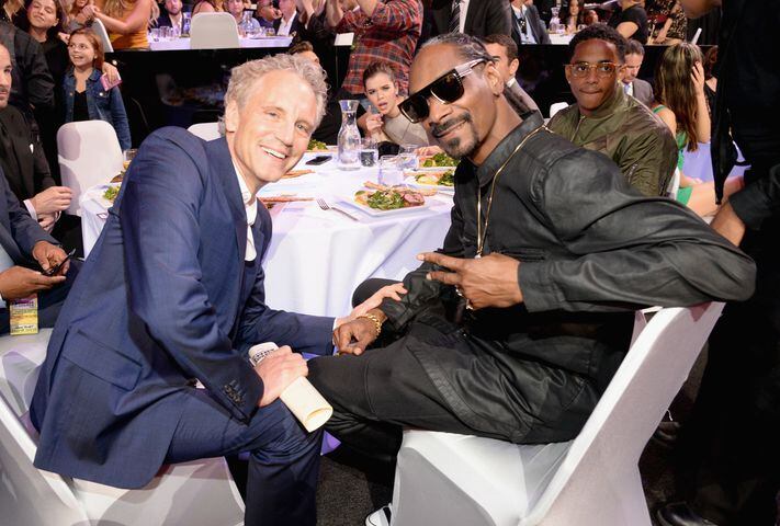 Hailee Stanfield (C) photobombs while Clear Channel Entertainment Enterprises President John Sykes (L) and rapper Snoop Dogg