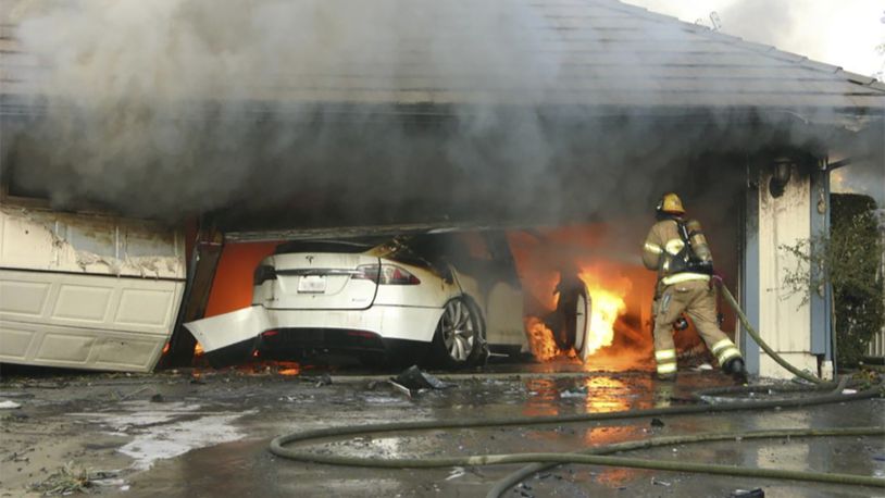 This undated photo provided by National Transportation Safety Board, The Orange County Fire Authority battles a fire on a burning vehicle inside a garage in Orange County, Calif.  When firefighters removed the SUV from the garage to assess the fire , they identified the fuel source as the SUV’s high-voltage battery pack.  U.S. safety investigators say electric vehicle fires pose risks to first responders, and manufacturers have inadequate guidelines to keep them safe. (Orange County Sheriff’s Department/National Transportation Safety Board via AP)