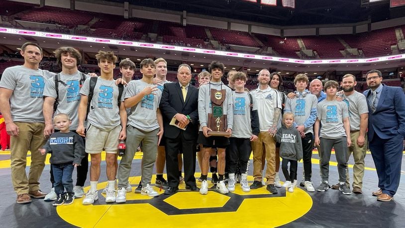 The Legacy Christian wrestling team led by coach Michael Sizemore (center) and three-time individual champion Dillon Campbell (holding trophy) won its third straight Division III team title Sunday at the Schottenstein Center in Columbus. CONTRIBUTED/Legacy Christian Academy