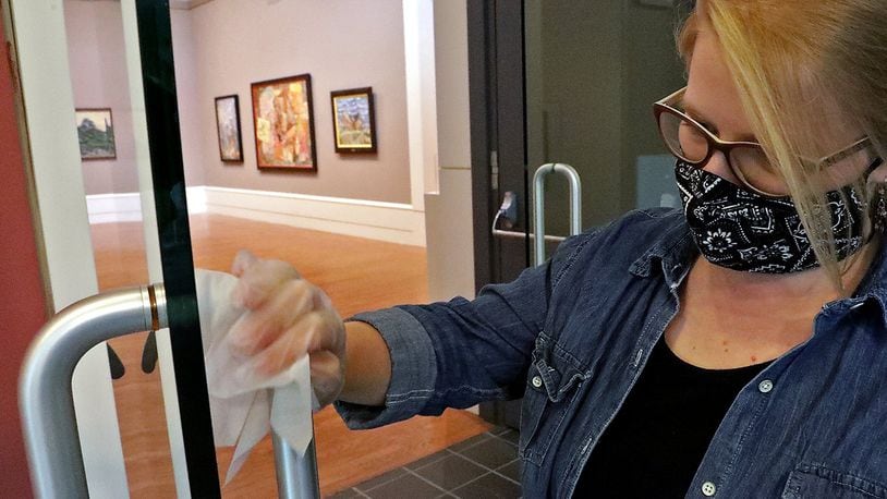 Elizabeth Wetterstroem wipes down door handles on the entry to the galleries at the Springfield Museum of Art in preparation of reopening in July. The museum closed again as coronavirus cases increased. The museum has reopened with new safety precautions. BILL LACKEY/STAFF