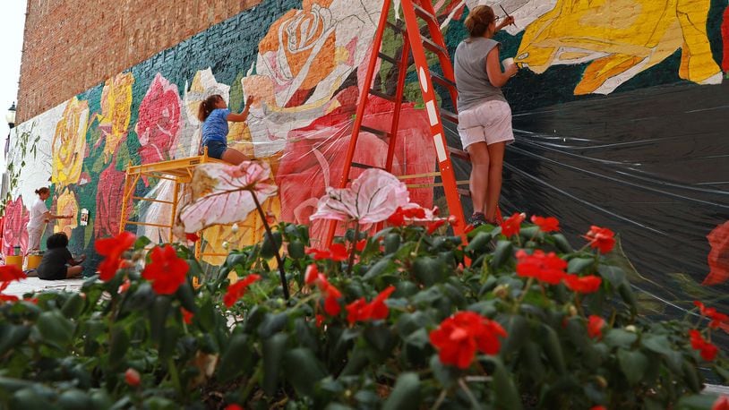 Members of Project Jericho work with artist Mariah Kaminsky to create the Rose City Mural in on the side of a building downtown Springfield Friday. The mural harkens back to when Springfield was called the Rose City because it produced more roses than anywhere else. BILL LACKEY/STAFF