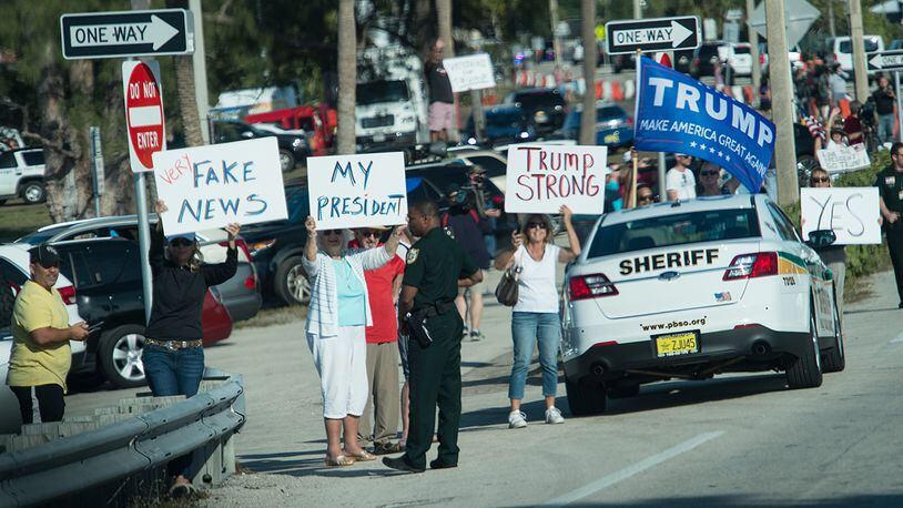 Supporters of US President Donald Trump hold signs as his motorcade drives by in Palm Beach, Florida, near his Mar-a-Lago resort on February 17, 2017. / AFP / NICHOLAS KAMM (Photo credit should read NICHOLAS KAMM/AFP/Getty Images)