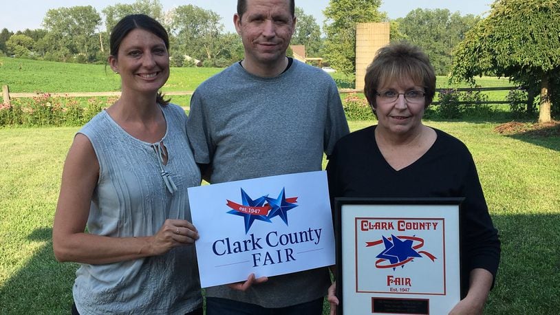 When Marin Smith, left, found out the Clark County Fair was going to update the logo designed by her mother-in-law, Rose, right, who is holding it, she couldn’t think of a better person to do it than her own husband and Rose’s son Jarid, center, shown holding the updated version. Photo courtesy of Marin Smith