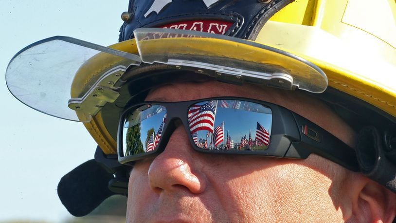 The field of American flags is reflected in the sunglasses of Fire Fighter Nathan Ryman, of the Rosewood Fire Department, Saturday during a 9/11 Remembrance Ceremony at Freedom Grove in Urbana. BILL LACKEY/STAFF