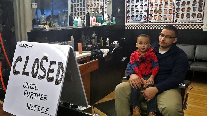 Alex Robinson, owner of Robinson Corner Cuts, and his son, Jarred, sit in his empty barber shop Thursday after the governor ordered all barber shops and nail salons to close Wednesday due to the coronavirus. BILL LACKEY/STAFF