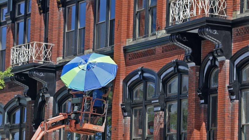 A painting crew uses a beach umbrella to provide a little shade while they paint the trim around windows of a building along North Main Street in Urbana in this August 2022 file image. The former Willman Furniture buildings will become a co-working and living space, in part because of state tax credits. BILL LACKEY/STAFF