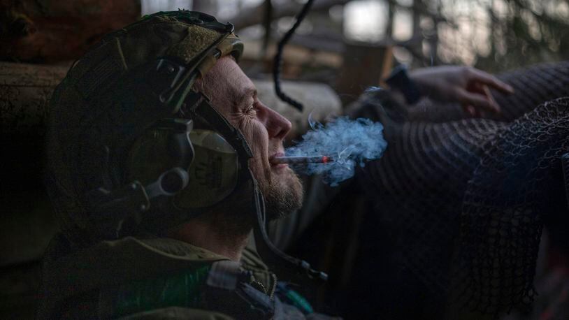 A Ukrainian serviceman from the Azov brigade, known by the call sign Chaos, smokes a cigarette while he waits for a command to fire, in a dugout around one kilometer away from Russian forces on the frontline in Kreminna direction, Donetsk region, Ukraine, Friday, April 12, 2024. (AP Photo/Alex Babenko)