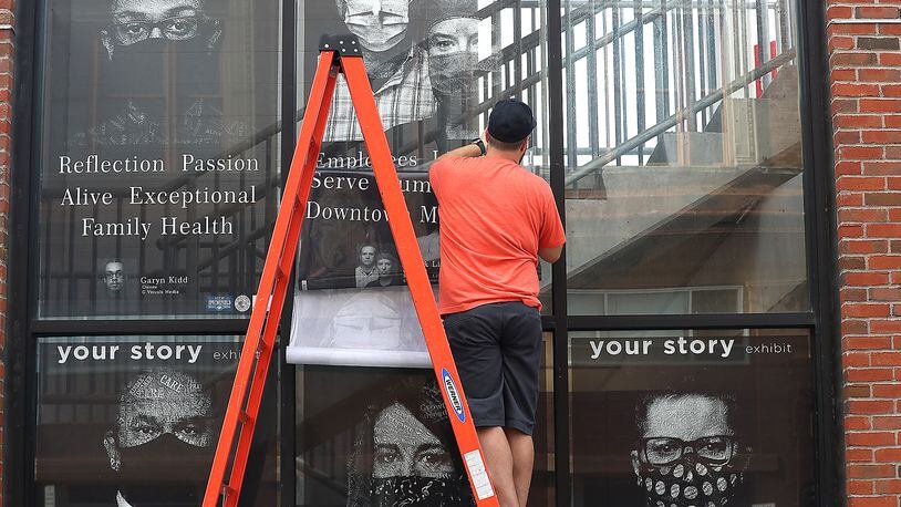 A worker from the MacRay Company attaches pictures for the "Your Story" art exhibit to the windows of the city parking garage earlier this month. The exhibit, by Ty Fischer, is made up of black and white photographs of community members scattered around downtown Springfield. BILL LACKEY/STAFF