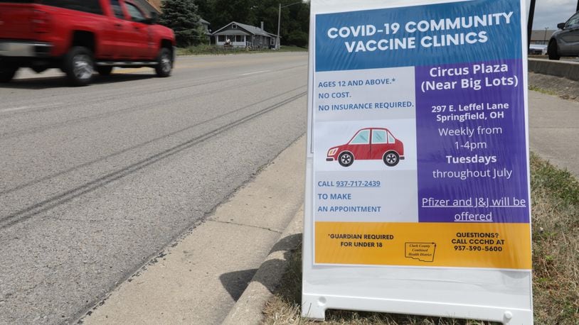 Cars drive past a sign for a free drive-thru COVID-19 vaccine clinic in the Circus Plaza on East Leffel Lane. BILL LACKEY/STAFF