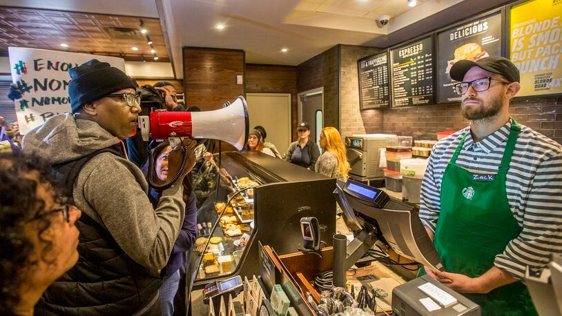Local Black Lives Matter activist Asa Khalif, left, stands inside the Starbucks at 18th and Spruce, and over a bullhorn, demands the firing of the manager that called police, which resulted in two black men being arrested. On Sunday April 15, 2018, protesters demonstrated outside the Starbucks and planned to return Monday. (Michael Bryant//Philadelphia Inquirer/TNS)