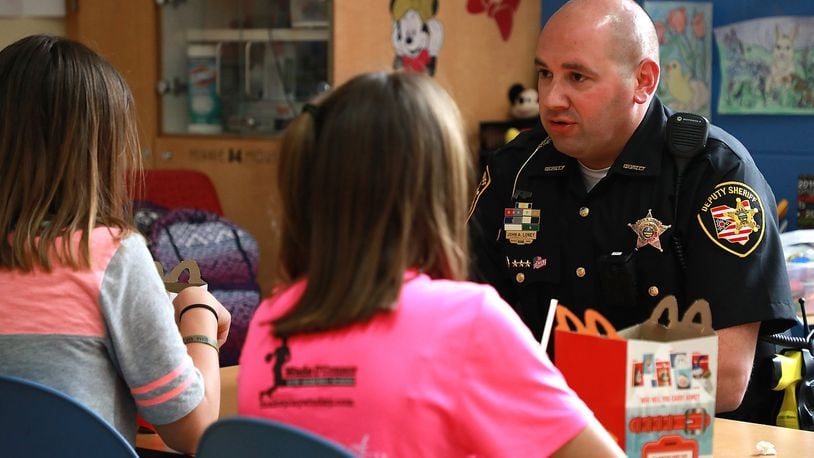 Deputy John Loney, the school resource officer for the Tecumseh School District, provides a caring ear along with lunch for two students going through a stressful time at home in May 2019. BILL LACKEY/STAFF