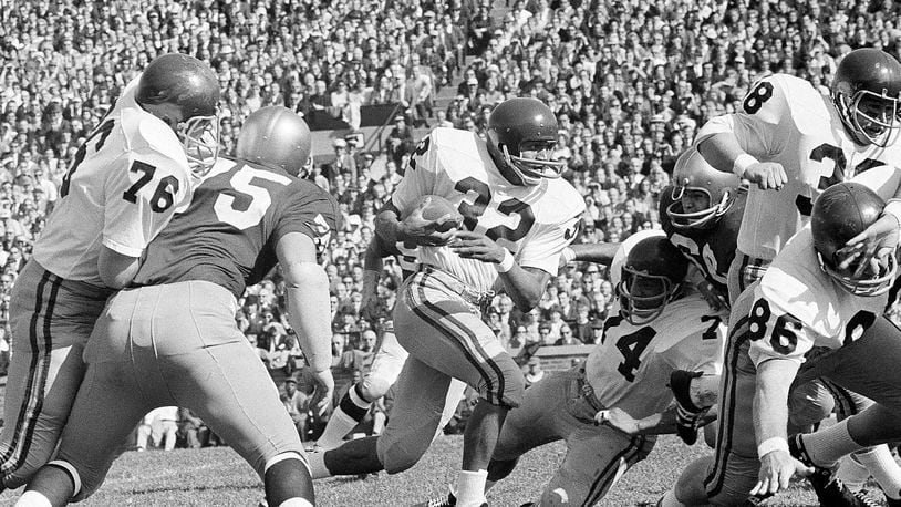 FILE - University of Southern California runningback O.J. Simpson (32)runs against Notre Dame Notre Dame in the first half of an NCAA college football game in South Bend, ind., Oct. 14, 1967. and picks up a few yards in their intersectional football game, Oct. 14, 1967 in South Bend, Indiana. Blocking for USC are Bob Miller (86), Mike Taylor (74), and Dan Scott (38). O.J. Simpson, the decorated football superstar and Hollywood actor who was acquitted of charges he killed his former wife and her friend but was found liable in a separate civil trial, has died. He was 76. The family announced on Simpson's official X account that he died Wednesday, April 10, 2024, of prostate cancer.(AP Photo/File)