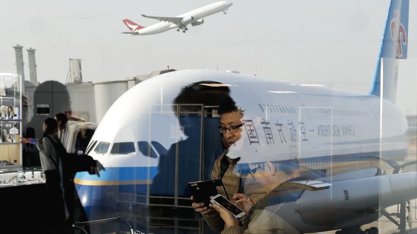 FILE - Passengers walk past a couple browsing their smartphones near a China Southern Airlines, parked on the tarmac at the Beijing Capital International Airport Saturday, Nov. 19, 2016. The biggest U.S. airlines and their unions are asking the Biden administration in a letter Thursday, April 11, 2024, to stop approving more flights to the United States by Chinese airlines. (AP Photo/Andy Wong, File)