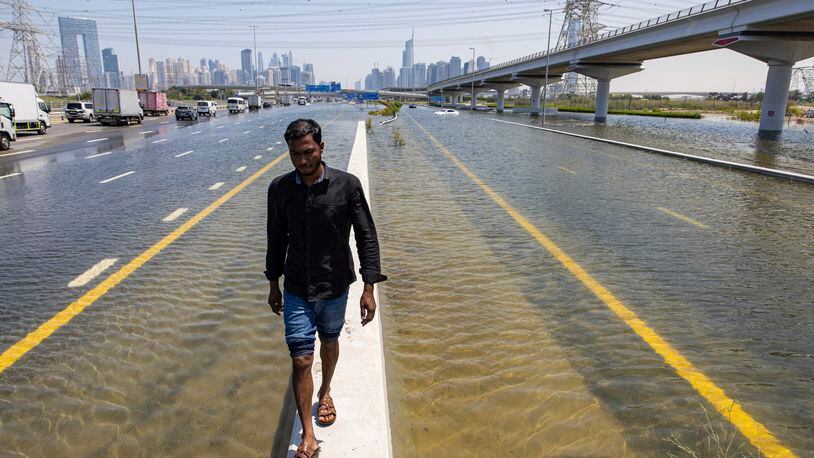 A man walks along a road barrier among floodwater caused by heavy rain on Sheikh Zayed Road highway in Dubai, United Arab Emirates, Thursday, April 18, 2024. The United Arab Emirates attempted to dry out Thursday from the heaviest rain the desert nation has ever recorded, a deluge that flooded out Dubai International Airport and disrupted flights through the world's busiest airfield for international travel. (AP Photo/Christopher Pike)