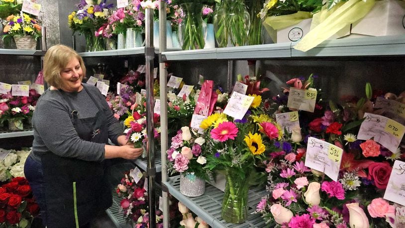 Amy Galbreath sets a flower arrangement in the cooler with dozens of others Thursday at Schneider's Florist. Schneider's is not facing a flower shortage, but many other local florists are. BILL LACKEY/STAFF