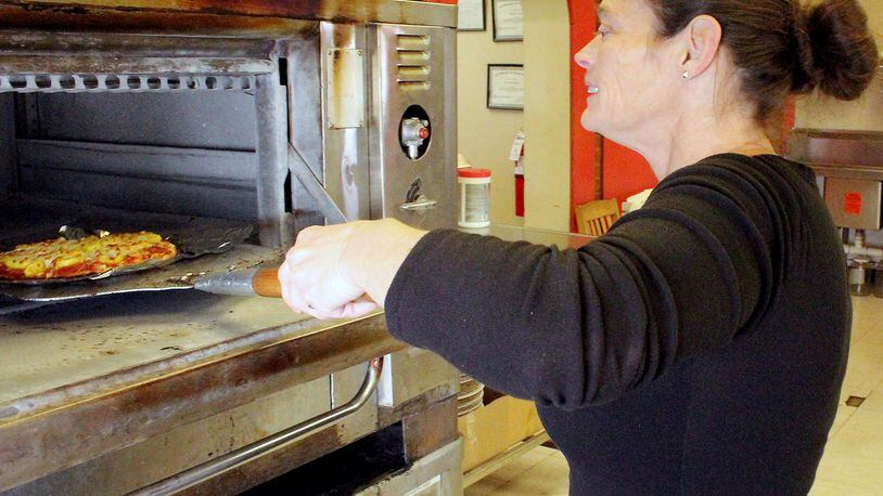Enon Pizza and Company owner Tracy Wiggins checks to see if a pizza is done cooking. JEFF GUERINI/STAFF