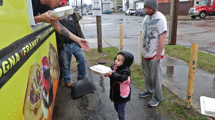 Rae’lyn Moore, 4, gets a free meal from Kim Poole, owner of Freddie’s Franks & Burgers food truck, Wednesday. Due to the coronavirus, the Springfield Soup Kitchen is not allowed to open, so they got Kim and her husband, Fred, to park their food truck in the parking lot across the street from the soup kitchen and are feeding people outdoors. BILL LACKEY/STAFF