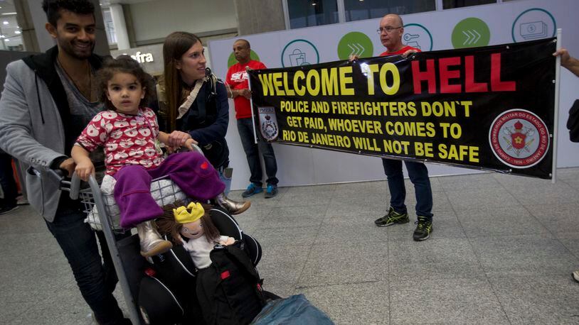 A family arrive to Brazil, while they walk past a banner that reads "Welcome to hell" during a police protest, demanding their payments and better labor conditions, at the Tom Jobim International Airport, in Rio de Janeiro, Brazil, Monday, July 4, 2016. Brazil is suffering the worst recession in decades and Rio's acting governor has declared a state of financial disaster this month, largely to bolster spending on security as the world's spotlight turns to the city. (AP Photo/Silvia Izquierdo)