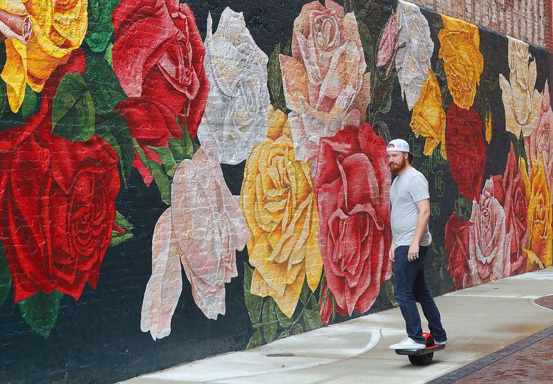Aaron Jernigan rides his One Wheel electric skateboard past the Rose City mural along Main Street in Springfield.  BILL LACKEY/STAFF