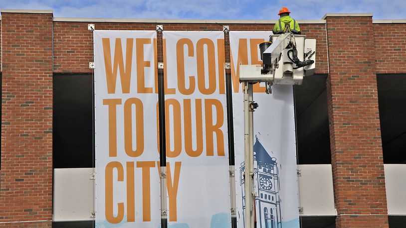 A City of Springfield service department employee uses a lift to hang a new banner on the Fountain Avenue side of the Park at the 99 parking garage Wednesday, April 3, 2024. BILL LACKEY/STAFF