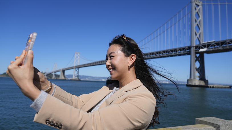 Content creator Cynthia Huang Wang works below the San Francisco-Oakland Bay Bridge in San Francisco, Monday, April 8, 2024. Despite a strong job market, there are still thousands of people who have found themselves out of work across industries stretching from tech to retail to media. But rather than trying to find another job in their old role, some workers are turning to online content creation. (AP Photo/Eric Risberg)