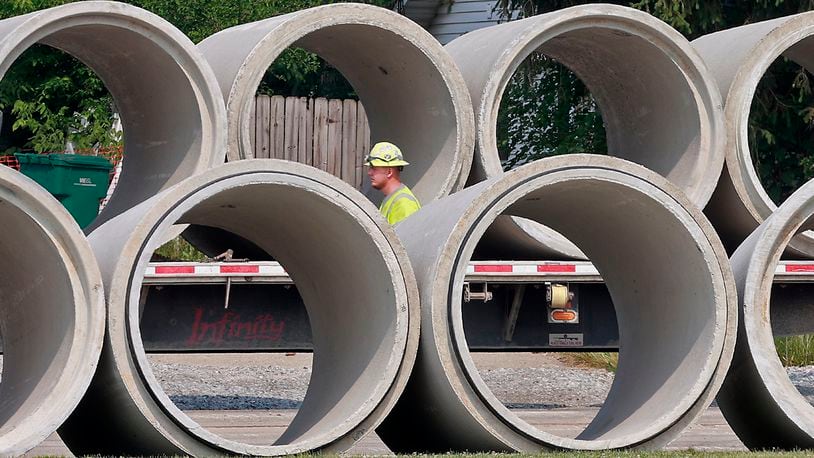A construction worker walks past a row of concrete culverts as he prepares to unload more from a flatbed semi trailer on Enon-Xenia Road in front of Greenon School Wednesday, June 7, 2023. BILL LACKEY/STAFF