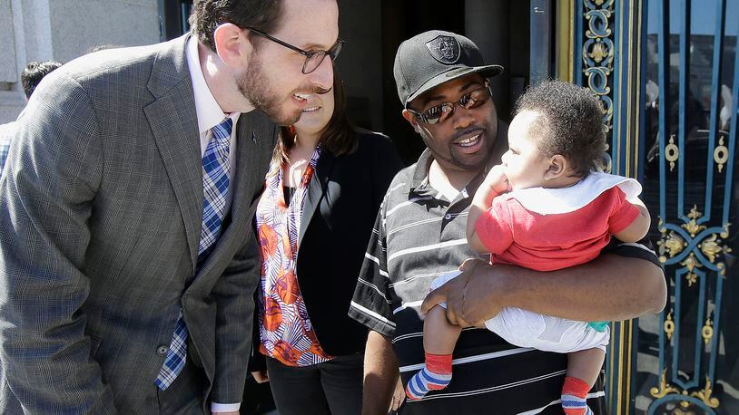 Alphonzo Jackson, center, holds his six-month old son Isaiah as he speaks with San Francisco Supervisor Scott Wiener, left, before a rally supporting paid family leave at City Hall in San Francisco on April 5, 2016.