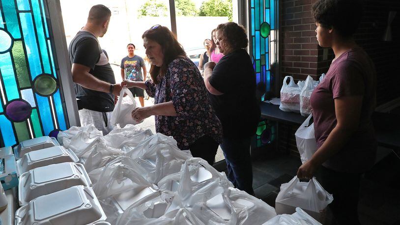 Kelly Myers, center, a H.O.P.E. volunteer, passes out free meals with other volunteers Wednesday. H.O.P.E, a nonprofit organization in Springfield, has served over 15,000 meals since the beginning of the coronavirus pandemic. BILL LACKEY/STAFF