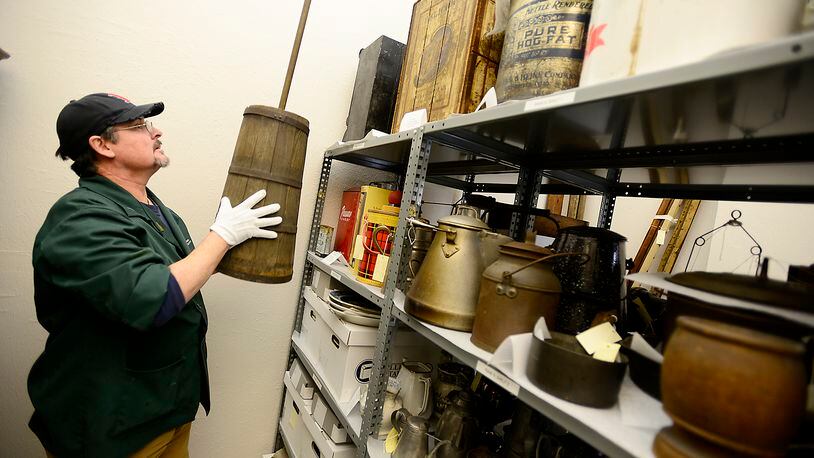 Mel Glover places an antique butter churn on a shelf as he organizes some of the items in the Clark County Historical Society’s collection of artifacts. The society has teamed up with several other organizations to offer an antique appraisal fair. Bill Lackey/Staff