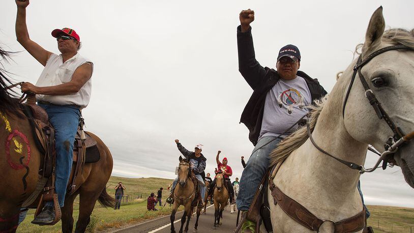 Native Americans ride with raised fists to a sacred burial ground that was disturbed by bulldozers building the Dakota Access Pipeline (DAPL), near the encampment where hundreds of people have gathered to join the Standing Rock Sioux Tribe's protest of the oil pipeline slated to cross the nearby Missouri River, September 4, 2016 near Cannon Ball, North Dakota. Protestors were attacked by dogs and sprayed with an eye and respiratory irritant yesterday when they arrived at the site to protest after learning of the bulldozing work. / AFP / ROBYN BECK (Photo credit should read ROBYN BECK/AFP/Getty Images)