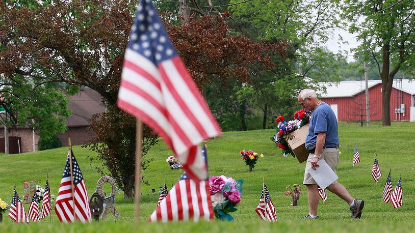 Don Lee, from Netts Floral Company and Greenhouse, carries a box full of red, white and blue flower arrangements Wednesday, May 24, 2023 as he walks through the sea of Amarican flags at Rose Hill Burial Park looking for the graves to place the flowers on.  BILL LACKEY/STAFF