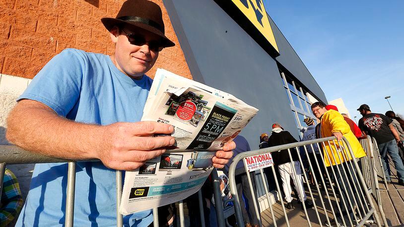 Josh Vanderpool reads the sale ads as he waits in line outside Best Buy in Springfield on Thanksgiving day. Several hundred people were waiting in line when the doors opened at 5 p.m. Thursday. Bill Lackey/Staff