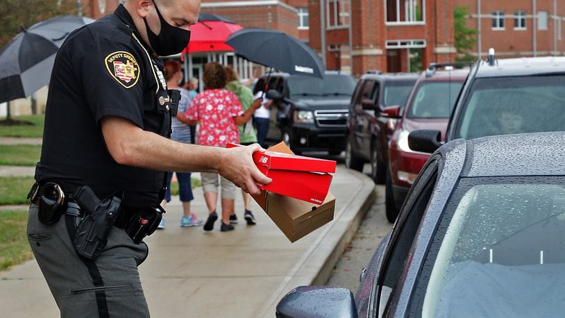 Clark County Sheriff's Deputy John Loney hands out boxes of shoes for children during the Shoes 4 the Shoeless drive thru event at Tecumseh High School Wednesday morning. BILL LACKEY/STAFF
