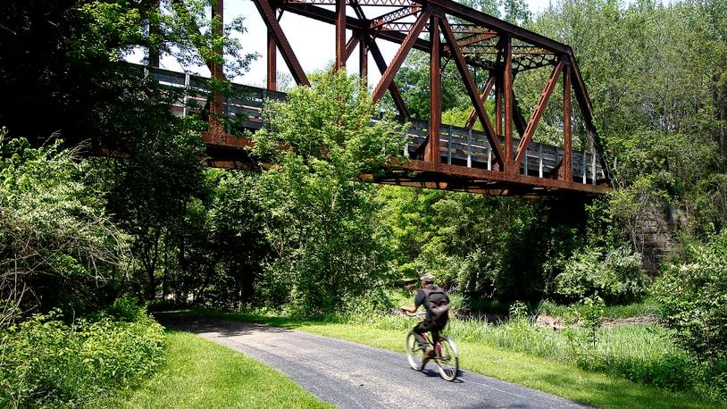 A man rides his bike under the Simon Kenton Trail bridge as he travels along the Buck Creek Trail Wednesday, May 8, 2024. The bridge was built in 1915. BILL LACKEY/STAFF