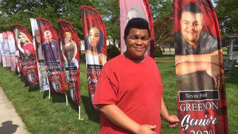 Tevin Pruitt stands next to his flag in Settlers’ Park in Enon. The flags are recognizing high school graduates in Mad River Twp., Enon and Green Twp. PAM COTTREL/CONTRIBUTOR
