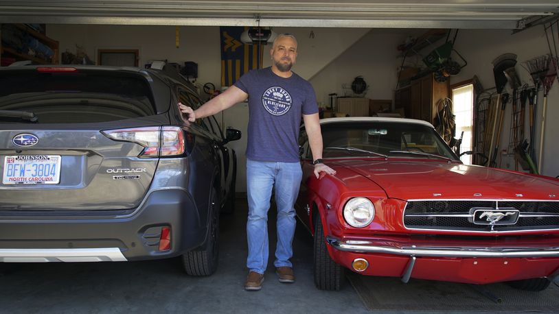 Steve Bock stands between his new Subaru Outback and his 1965 Ford Mustang at his home in Apex, N.C., on Friday, March 5, 2021. He would like to have an electric car, but says the prices will have to come down a lot before he can do it. Opinion polls show that most Americans would consider an EV if it cost less, if more charging stations existed and if a wider variety of models were available. (AP Photo/Allen G. Breed)