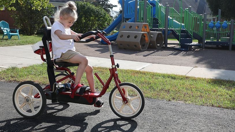 Lainey Wilson peddles a tricycle around the new paved walking path at the Mercy Health’s Pediatric Rehab playground Monday. BILL LACKEY/STAFF