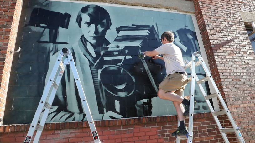 W.E. Arnold, along with Pete Hrinko and Shem Schutte, works on a mural of famous Springfield photographer Berenice Abbott on the exterior wall of Mother Stewart’s Brewery Sunday. BILL LACKEY/STAFF