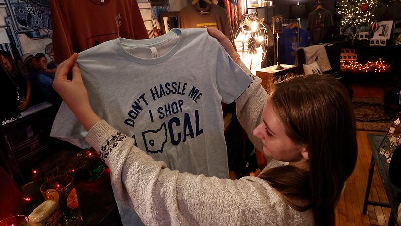 Malory Janicki looks at a shirt promoting shopping locally Tuesday, Nov. 22, 2022 at Champion City Guide and Supply in downtown Springfield. BILL LACKEY/STAFF