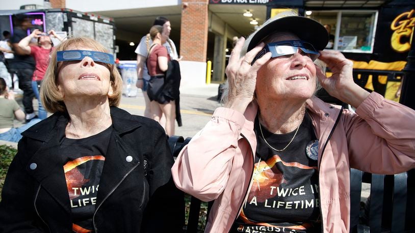 Mardi Briggs, left, and her sister, Randi Decious, both from California, watch the total eclipse Monday, April 8, 2024 at National Road Commons Park. The siblings said they were born in Springfield and hadn't been back in 70 years. BILL LACKEY/STAFF