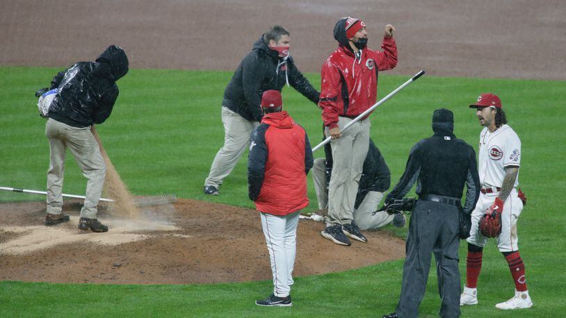 The Reds grounds crew works on the mound as manager David Bell, center, watches, just before the game was suspended by rain in the eighth inning on Tuesday, April 20, 2021, at Great American Ball Park in Cincinnati. David Jablonski/Staff