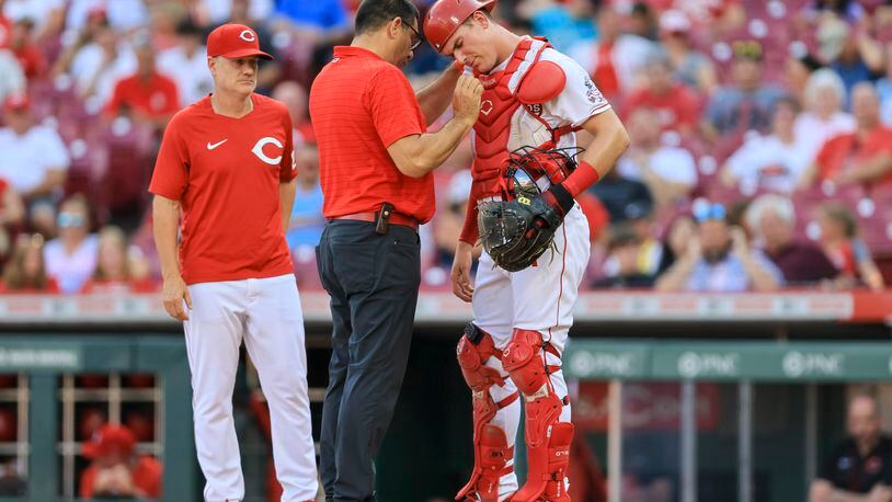 Cincinnati Reds' Tyler Stephenson, right, is checked by assistant athletic trainer Tomas Vera during the first inning of the team's baseball game against the St. Louis Cardinals in Cincinnati, Friday, July 22, 2022. (AP Photo/Aaron Doster)