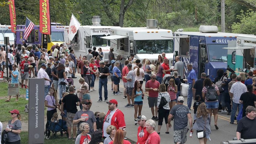 Hundreds of people walk up and down Cliff Park Drive eating from food trucks and watching Ohio State on a jumbotron screen Saturday during the Springfield Rotary Gourmet Food Truck Competition. BILL LACKEY/STAFF