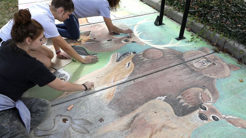 Cheyenne Combs, left, Ellie Shinkle, center, and Melissa Sherrock work on a chalk picture during Chalktoberfest at National Road Commons Park. Bill Lackey/Staff