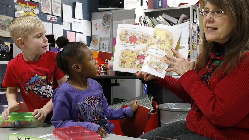 Liam Comley and Ja’Niyah Jones, students in Angie Caudill’s kindergarten class at Perrin Woods Elementery, follow along with tutor Jo Ann Cooper as she reads a story in class Thursday. Bill Lackey/Staff