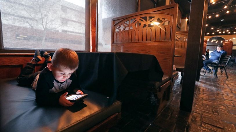 Callan Catanzaro, 3, plays on a phone Wednesday while his parents get their new restaurant, Fratelli's Famiglia Ristorante, ready for its grand opening. BILL LACKEY/STAFF