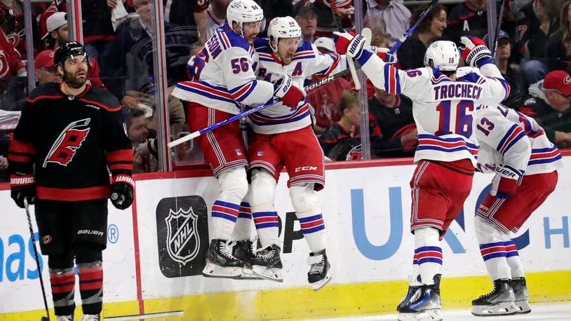New York Rangers defenseman Erik Gustafsson (56), left wing Artemi Panarin, center Vincent Trocheck (16) and left wing Alexis Lafrenière (13) celebrate after scoring the winning goal in the overtime period in Game 3 of an NHL hockey Stanley Cup second-round playoff series Thursday, May 9, 2024, in Raleigh, N.C. Carolina Hurricanes left wing Jordan Martinook skates away at left. (AP Photo/Chris Seward)
