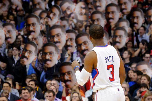 Los Angeles Clippers guard Chris Paul looks on as fans hold up pictures of him.