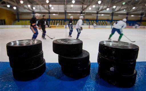 Hockey pucks are stacked on the boards as Vancouver Canucks players skate past during an informal NHL hockey practice.